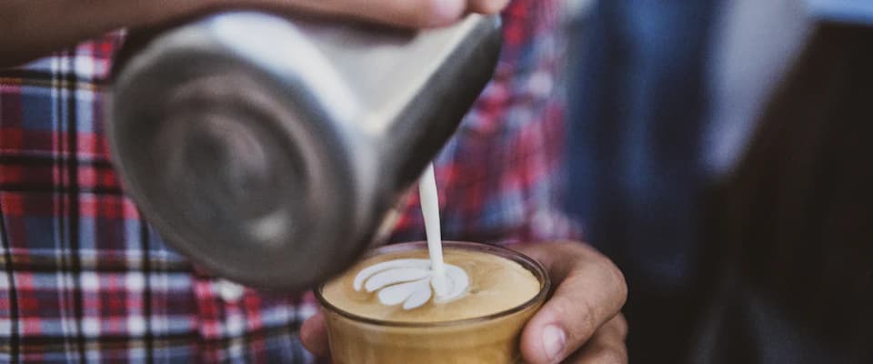 Barista pouring latte art into a glass of coffee