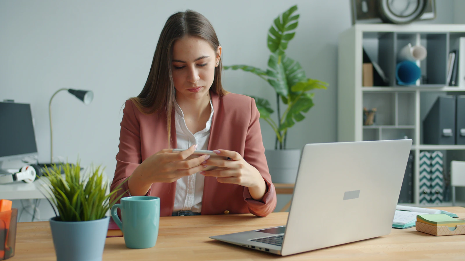 Woman at her desk checking her phone next to a laptop